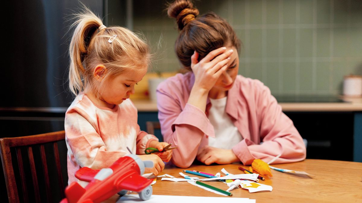 Vyčerpaná matka sedí u stolu s hlavou v dlaních